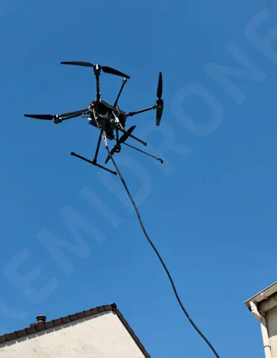Drone volant avec câble au-dessus de maisons.