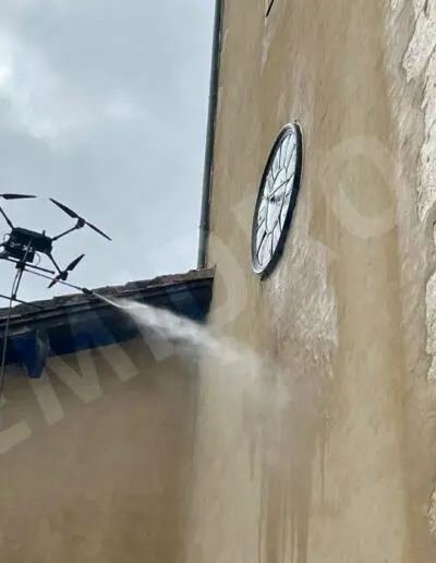 Drone nettoyant façade murale avec une horloge visible.