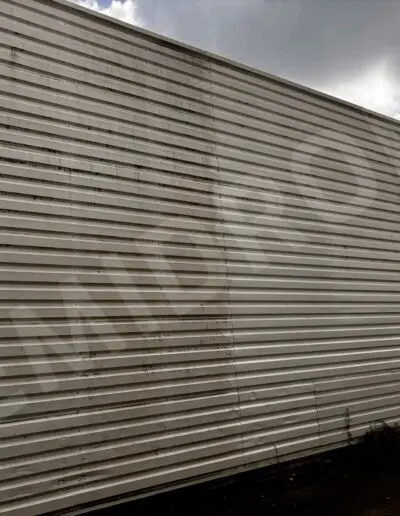 Mur de bardage métallique rayé, ciel nuageux.