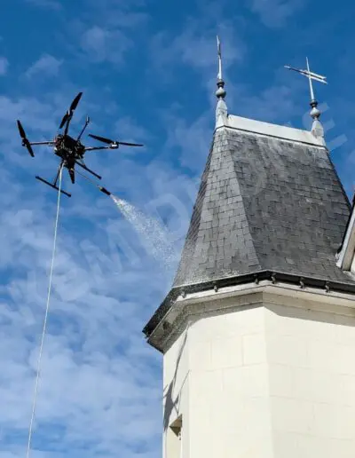 Drone nettoyant toit ardoise église, ciel bleu.