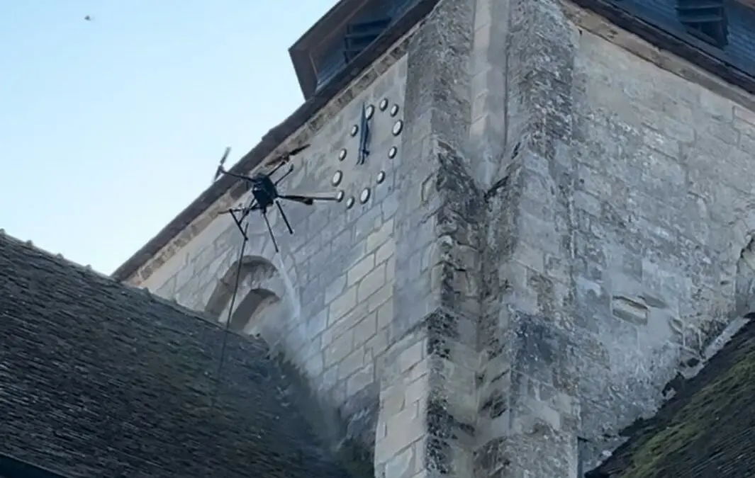 Drone professionnel pulvérisant des solutions de nettoyage et démoussage sur toiture en tuiles et ardoises, intervention rapide et sécurisée dans tout le département Essonne (91).