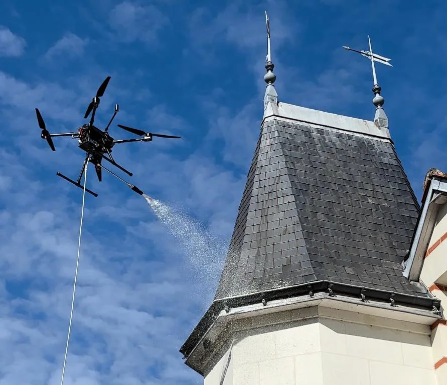 Drone multirotor pulvérisant une fine brume près du toit en ardoise d’une petite tour.